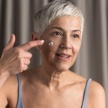 Woman applying face cream Beautiful mature woman with short gray hair putting some cream on her face, Skin care concept