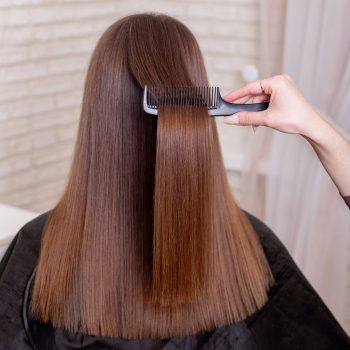 Hairdresser's hand brushing long brunette hair in beauty salon