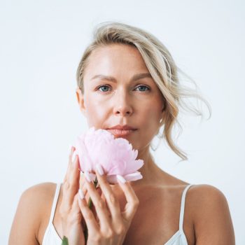 Beauty portrait of blonde hair smiling young woman with pink peony in hand isolated on white background Beauty portrait of blonde hair smiling young woman with pink peony in hand isolated on white background
